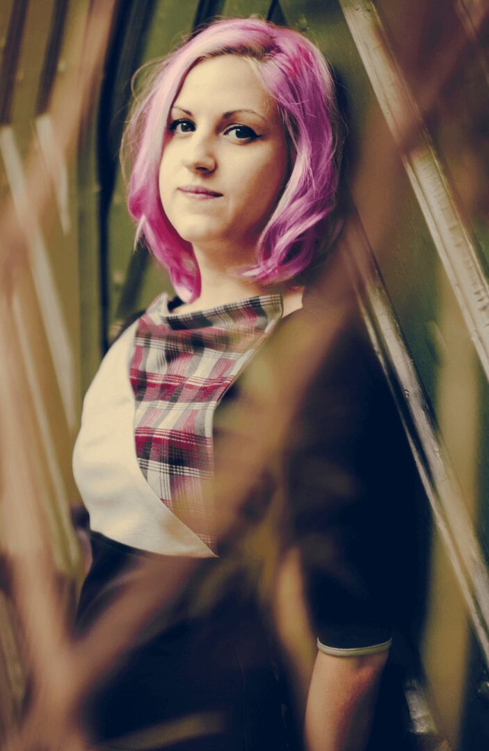 A woman with pink hair and a plaid scarf.